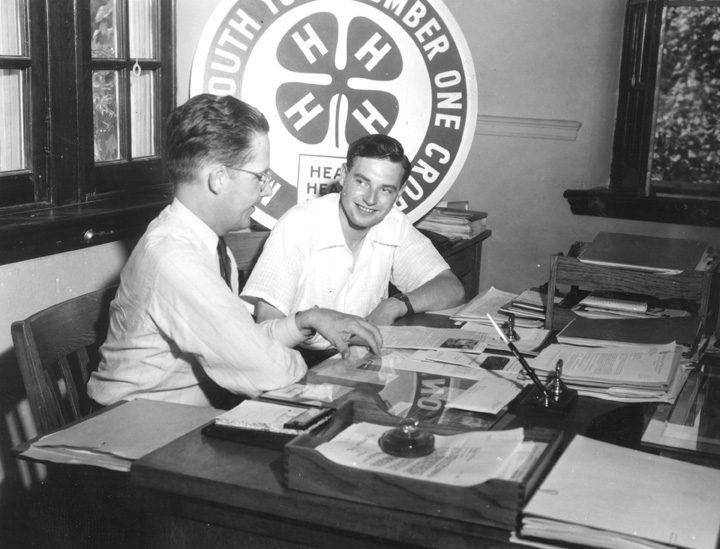 Historical image of two men in front of a 4-H banner